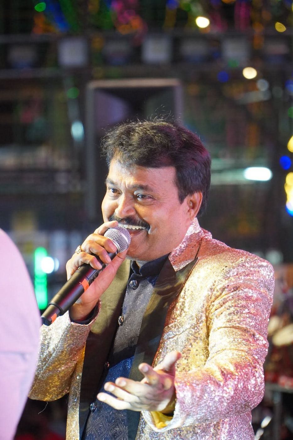 Ramu Maharajapuram singing on stage in a gold sequinned jacket