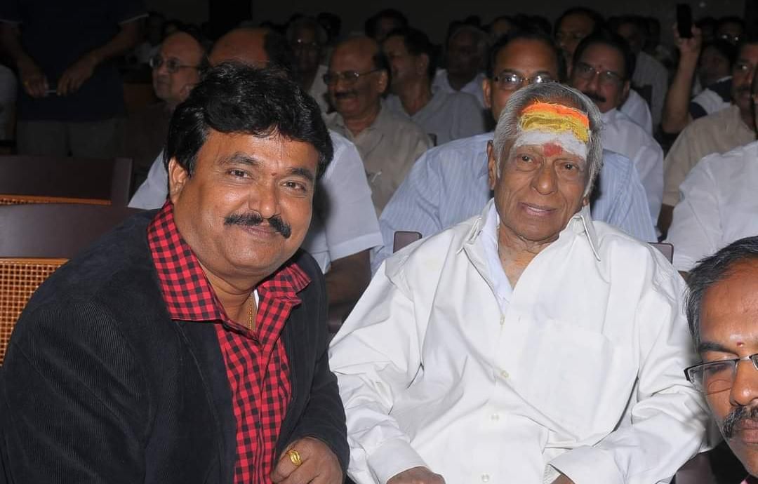 Ramu seated with a fellow artist at an event