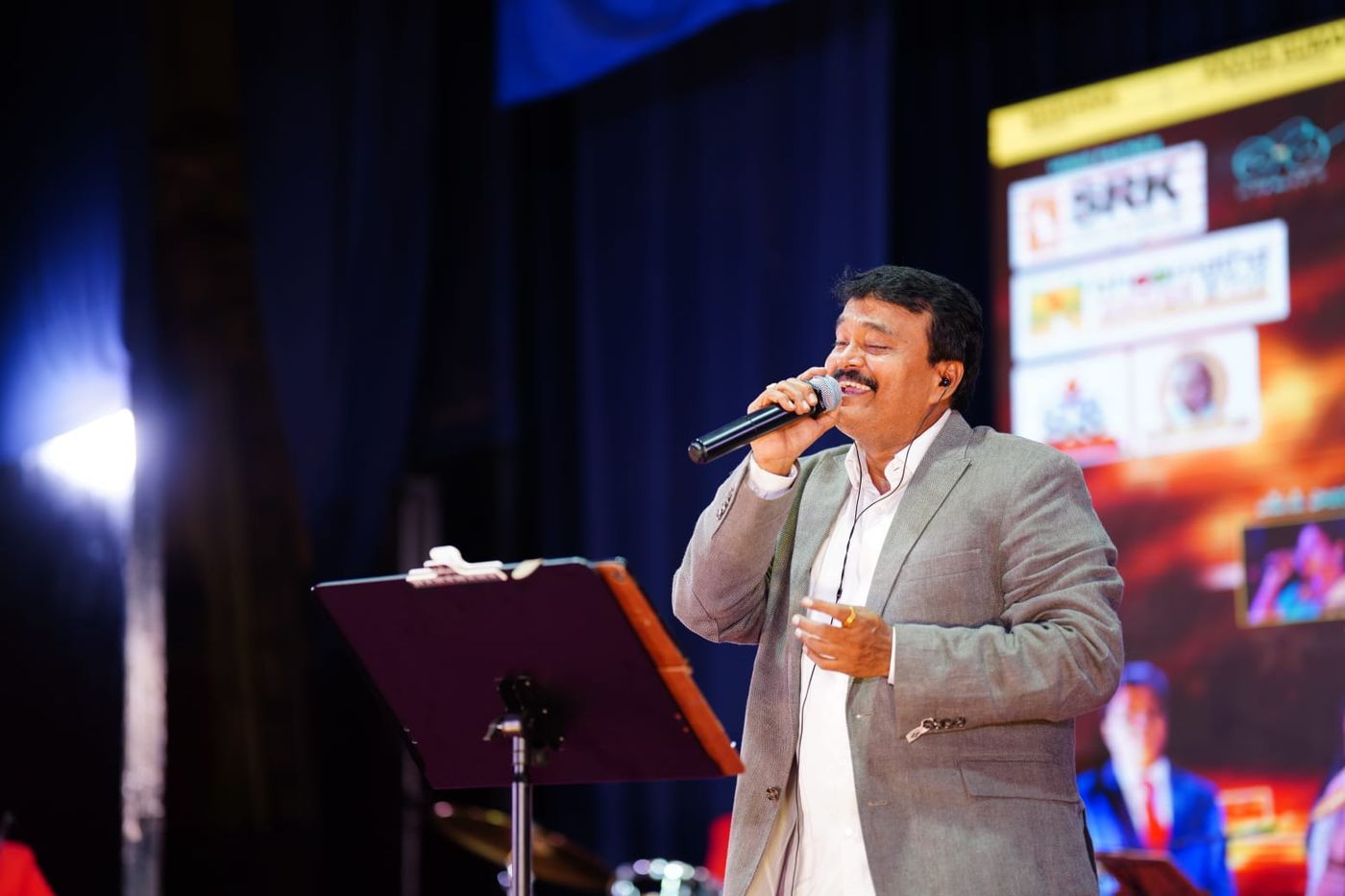 Ramu singing on stage in a beige blazer