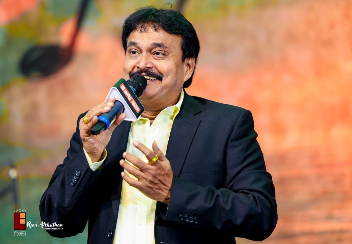 Ramu singing on stage in a black blazer