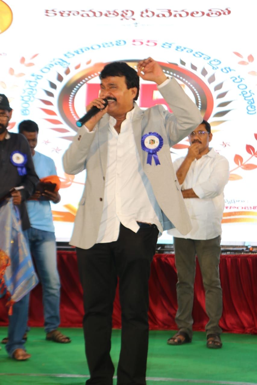 Ramu singing on an outdoor stage in a grey blazer
